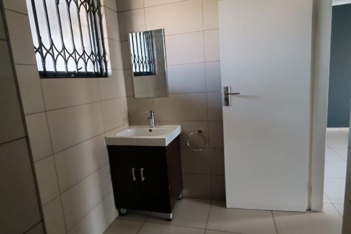 A clean, tiled bathroom featuring a modern vanity cabinet with a basin, wall mirror, and a window fitted with a security gate.