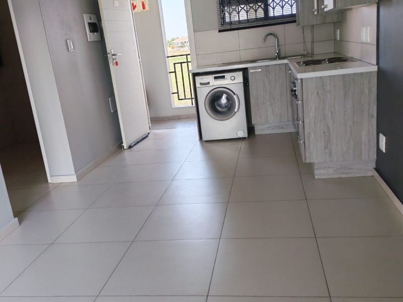 Open plan kitchen area featuring modern grey cabinetry, tiled flooring, and direct access to a balcony with security gate.