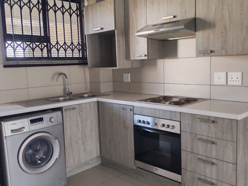 Modern kitchen featuring light wood-look cabinetry, integrated oven and hob, stainless steel sink, and tiled splashbacks with security bars on the window.