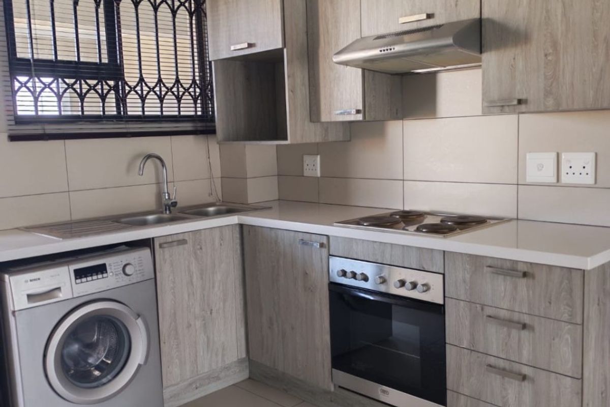 Modern kitchen featuring light wood-look cabinetry, integrated oven and hob, stainless steel sink, and tiled splashbacks with security bars on the window.