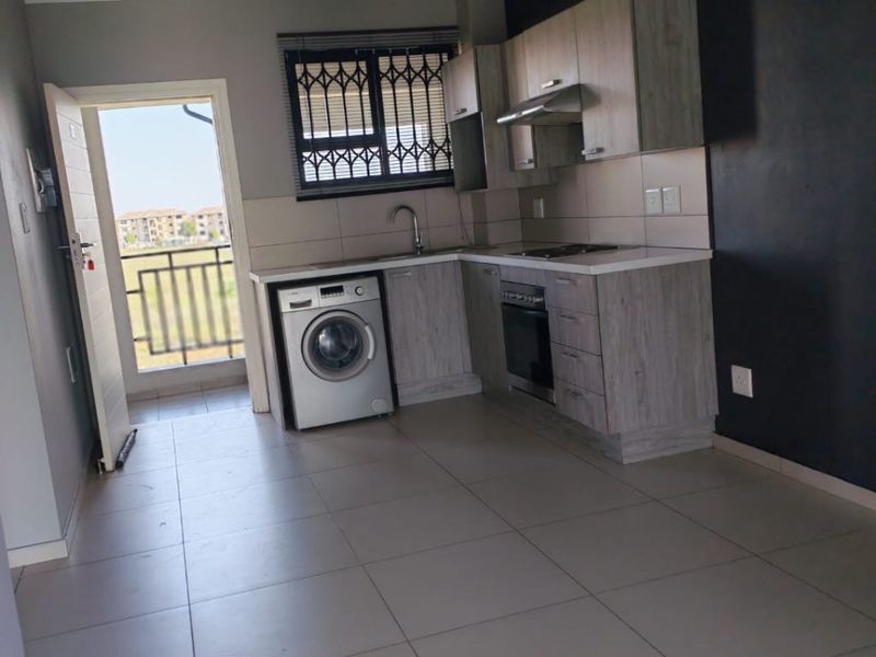 Compact kitchen featuring modern cabinetry, built-in oven, extractor fan, and tiled flooring, with direct access to an outdoor balcony area.