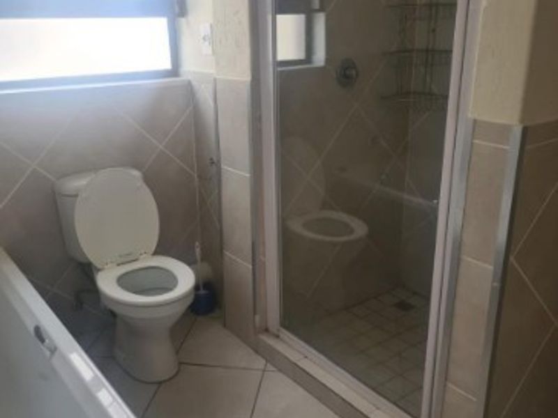 A functional bathroom featuring a bathtub, separate shower enclosure, and toilet with neutral wall and floor tiling.