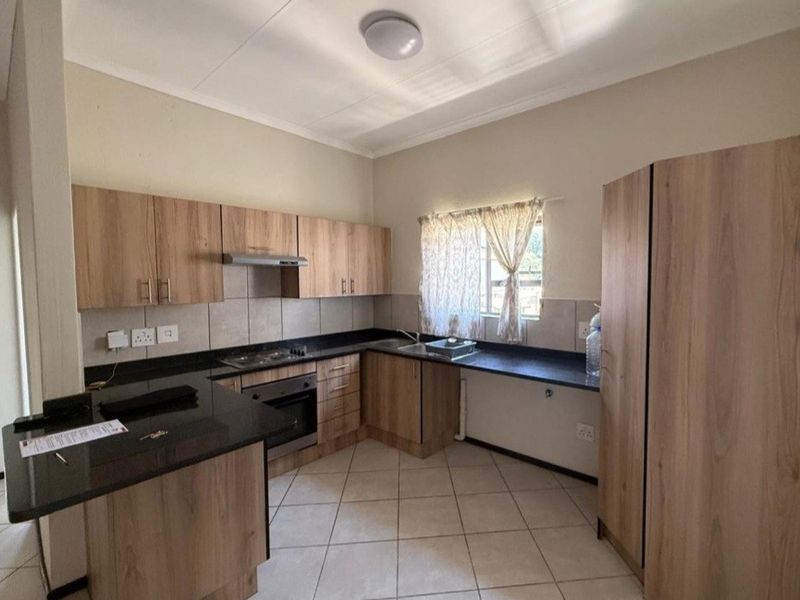 A functional kitchen featuring wood-look cabinetry, granite countertops, built-in oven, hob, extractor fan, and tiled flooring.