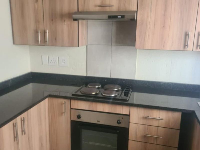 A functional kitchen featuring light wood-finish cabinetry, black granite countertops, and integrated appliances including an oven, hob, and extractor fan.