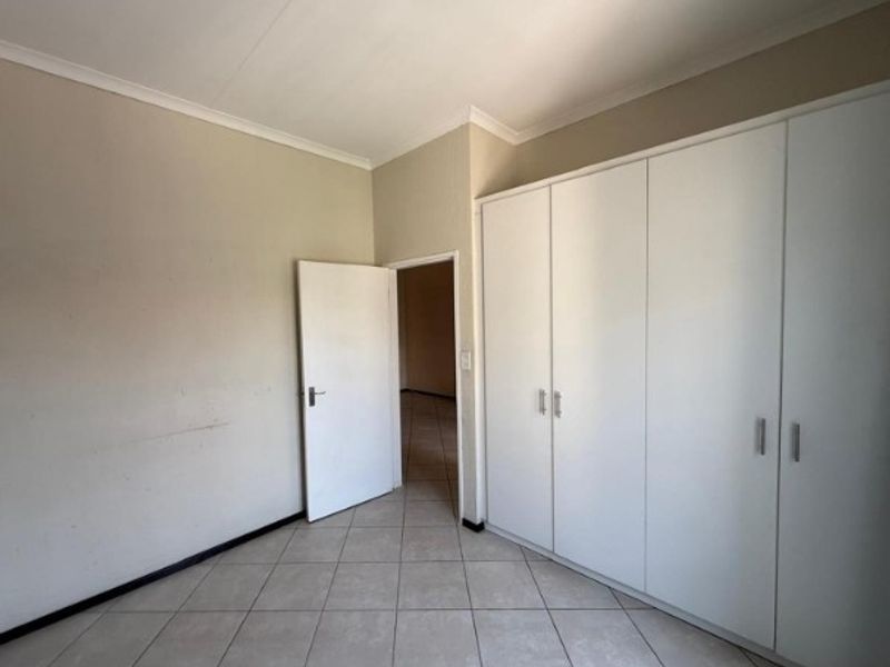 An empty bedroom featuring neutral tiled flooring, built-in white cupboards, and a doorway leading to an adjacent space.