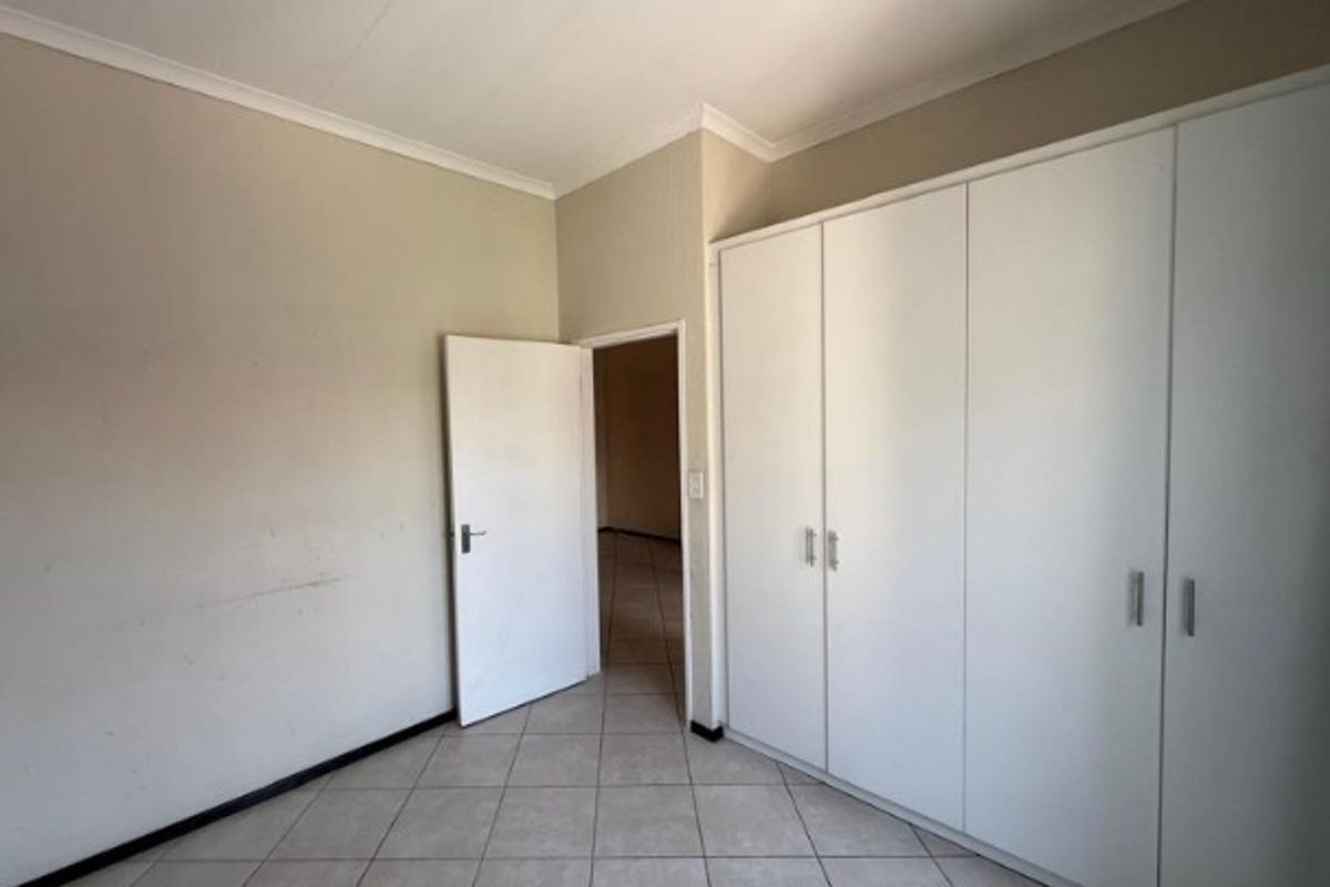 An empty bedroom featuring neutral tiled flooring, built-in white cupboards, and a doorway leading to an adjacent space.