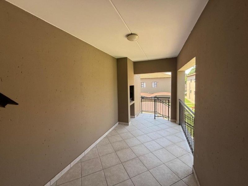 A spacious covered balcony featuring tiled flooring, a built-in braai, and metal balustrades, offering a functional outdoor entertainment area.