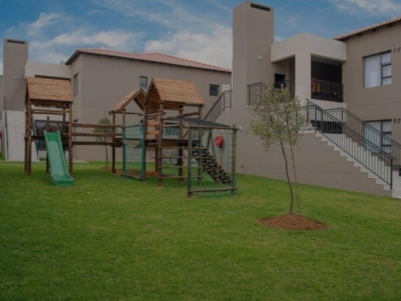 Exterior view of an apartment complex featuring a communal lawn, children's playground equipment, and external staircases leading to upper-level balconies.