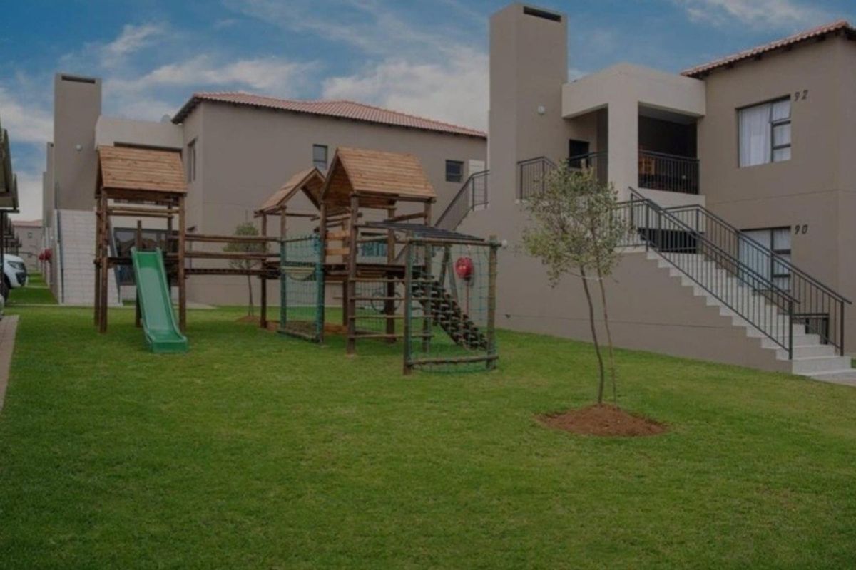 Exterior view of an apartment complex featuring a communal lawn, children's playground equipment, and external staircases leading to upper-level balconies.