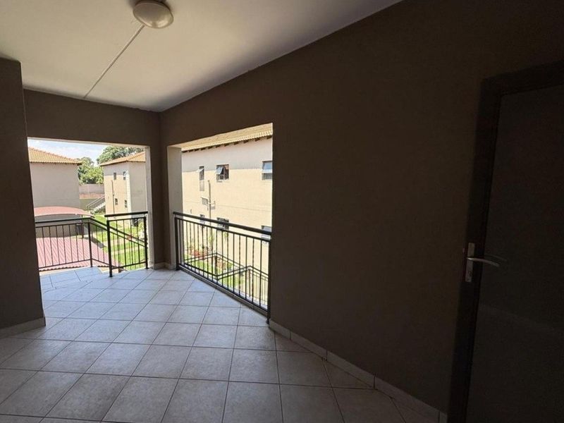 A covered balcony featuring tiled flooring and metal railings, offering an open outdoor space with views of the surrounding apartment complex.