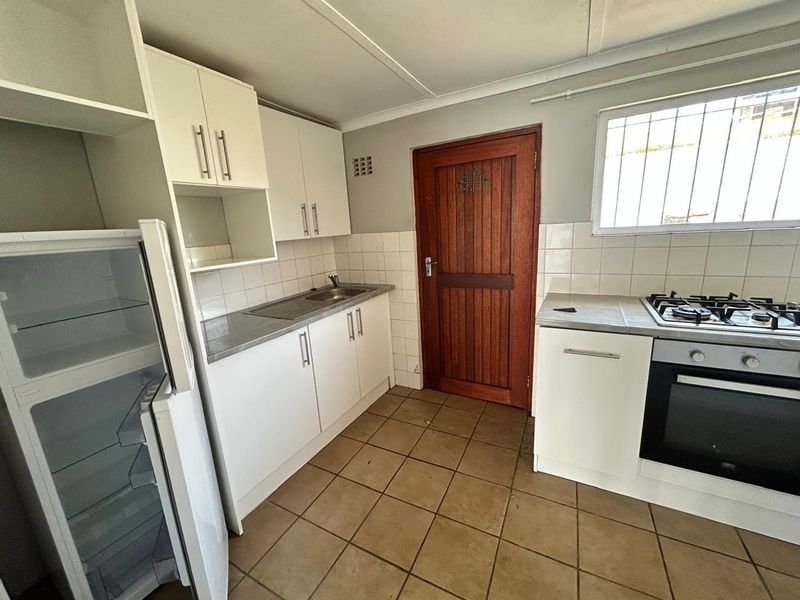 A functional kitchen featuring white cabinetry, stainless steel sink, gas hob, built-in oven, tiled splashback, and direct access via a timber door.