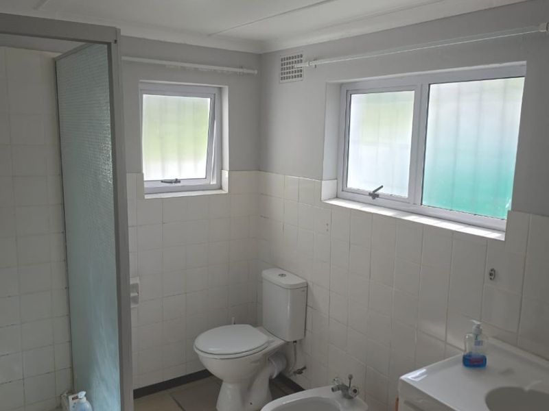 Functional bathroom featuring a shower enclosure, toilet, bidet, and vanity basin with tiled finishes and natural light from casement windows.