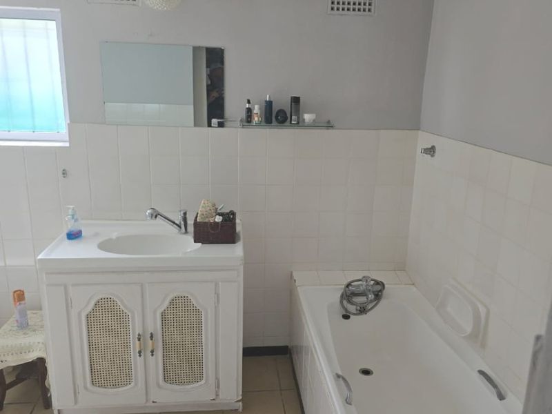 A functional bathroom featuring a vanity cabinet, bathtub, and tiled finishes. The space is dated and would benefit from modern updates.