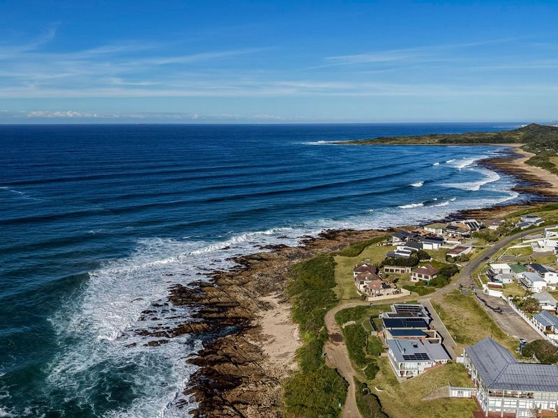 An aerial view of a coastal residential estate situated along the rocky shoreline, showcasing the proximity to the ocean and surrounding landscape.