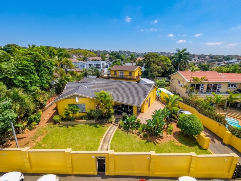 Aerial view of a residential property featuring a yellow exterior, tiled roof, landscaped garden, and a secure perimeter wall.