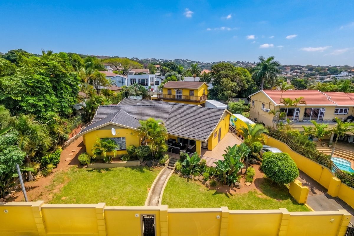 Aerial view of a residential property featuring a yellow exterior, tiled roof, landscaped garden, and a secure perimeter wall.