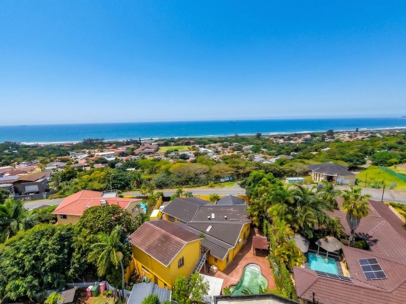 An elevated aerial view of the property showcasing the swimming pool, tiled roof structure, solar panels, and surrounding coastal neighborhood landscape.