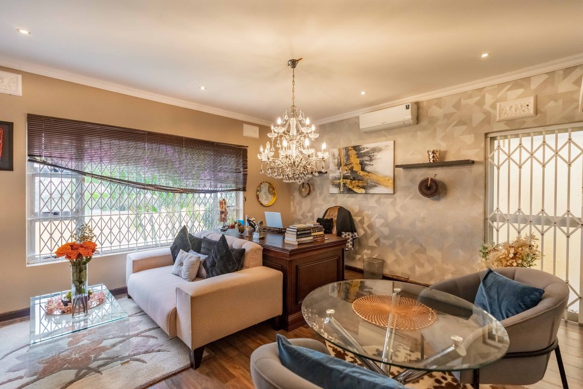 A well-maintained living area featuring laminate flooring, a decorative crystal chandelier, split-system air conditioning, and secure window and door treatments.
