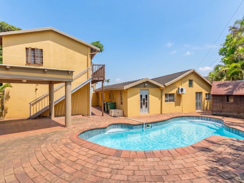 Rear exterior view featuring a swimming pool, paved patio area, covered outdoor space, and an external staircase leading to the upper level.