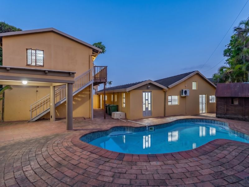 Rear exterior view featuring a swimming pool, brick paved patio area, external staircase leading to a balcony, and well-maintained building facades.