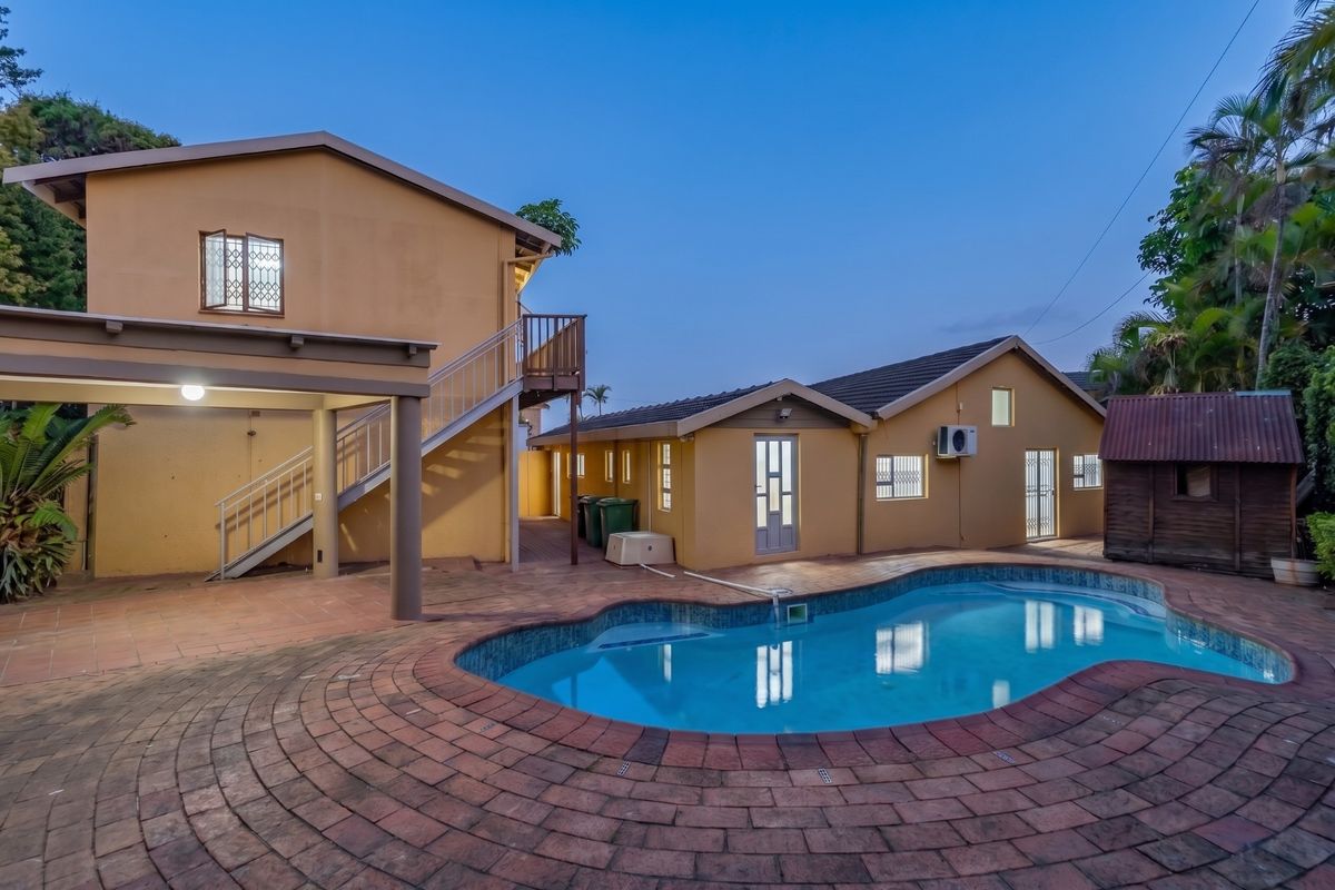 Rear exterior view featuring a swimming pool, brick paved patio area, external staircase leading to a balcony, and well-maintained building facades.