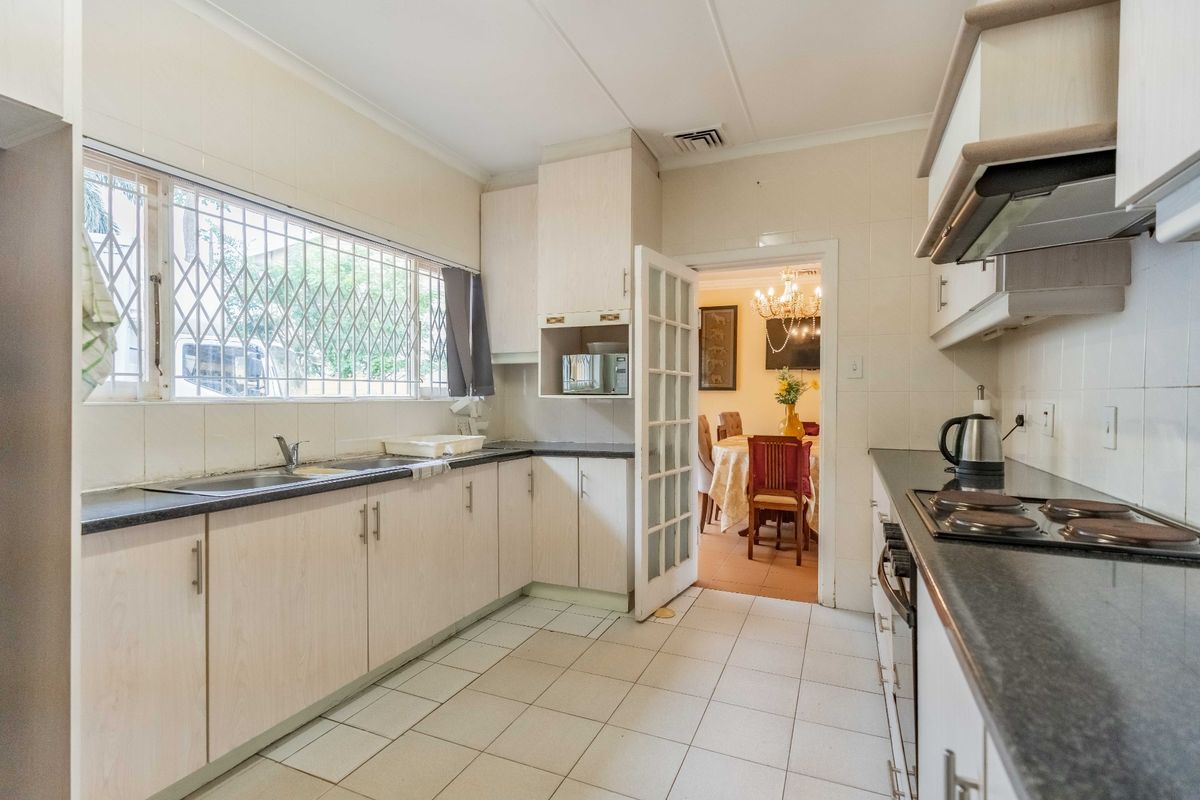 Functional kitchen featuring built-in cabinetry, laminate countertops, electric hob, extractor fan, and tiled flooring with a view into the adjacent dining area.