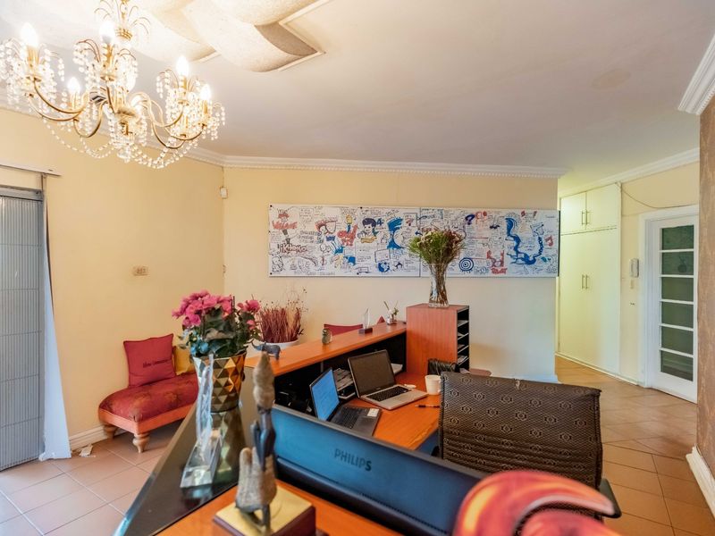 A functional office space featuring tiled flooring, crown molding, a crystal chandelier, and built-in storage cupboards with access to an outdoor patio area.