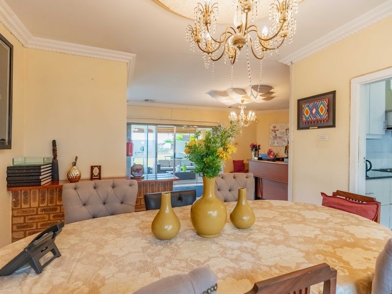 Open plan dining area featuring a crystal chandelier, crown molding, and a brick feature wall, with a view through to the kitchen and patio.