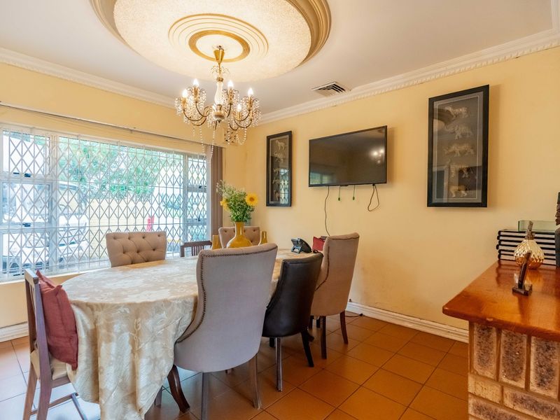 A dining room featuring tiled flooring, a decorative ceiling rose with a chandelier, and a large window fitted with a security gate.