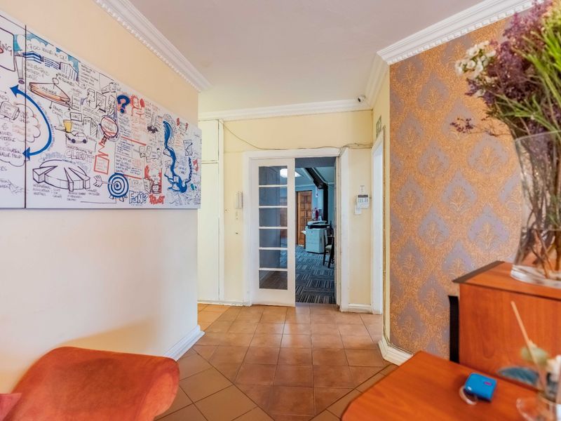 A tiled hallway featuring crown molding and a glass panel door leading to an adjacent room, with some visible wear on the door frame.
