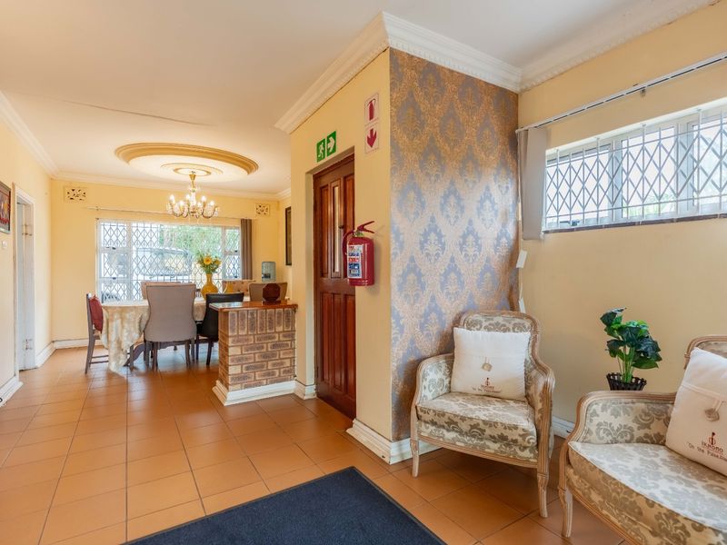 Open plan living and dining area featuring ceramic tile flooring, decorative ceiling details, and a brick feature wall with security-fitted windows.