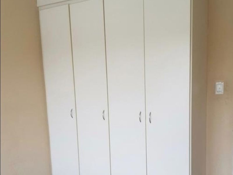 A clean bedroom featuring a large, white built-in wardrobe with modern handles and classic cornice detailing.