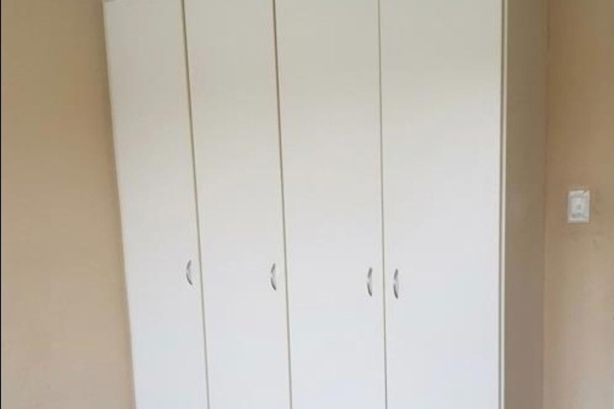 A clean bedroom featuring a large, white built-in wardrobe with modern handles and classic cornice detailing.