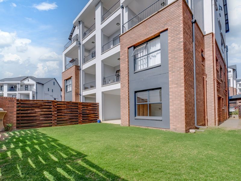 Rear view of a modern townhouse complex featuring a private lawn area, timber fencing, and multi-level balconies with brick and rendered finishes.