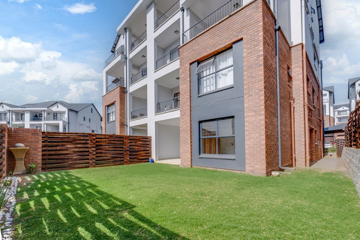 Rear view of a modern townhouse complex featuring a private lawn area, timber fencing, and multi-level balconies with brick and rendered finishes.