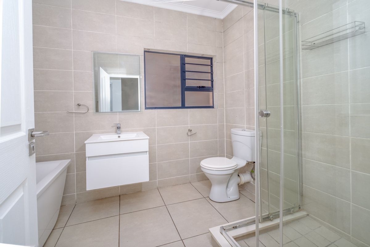 A clean, modern bathroom featuring a wall-mounted vanity, a separate shower enclosure, a bathtub, and neutral floor-to-ceiling wall tiles.