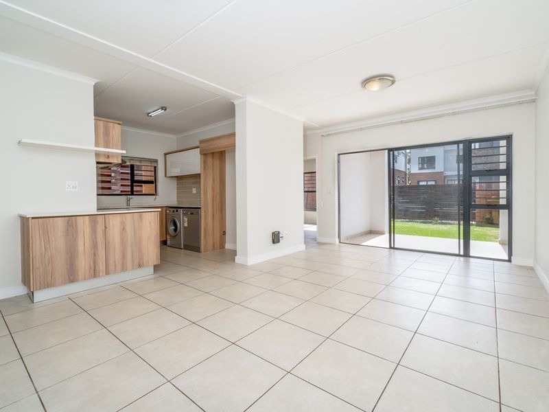 Spacious open-plan living area featuring tiled floors, modern kitchen cabinetry, and large sliding doors providing seamless access to the rear patio and garden.
