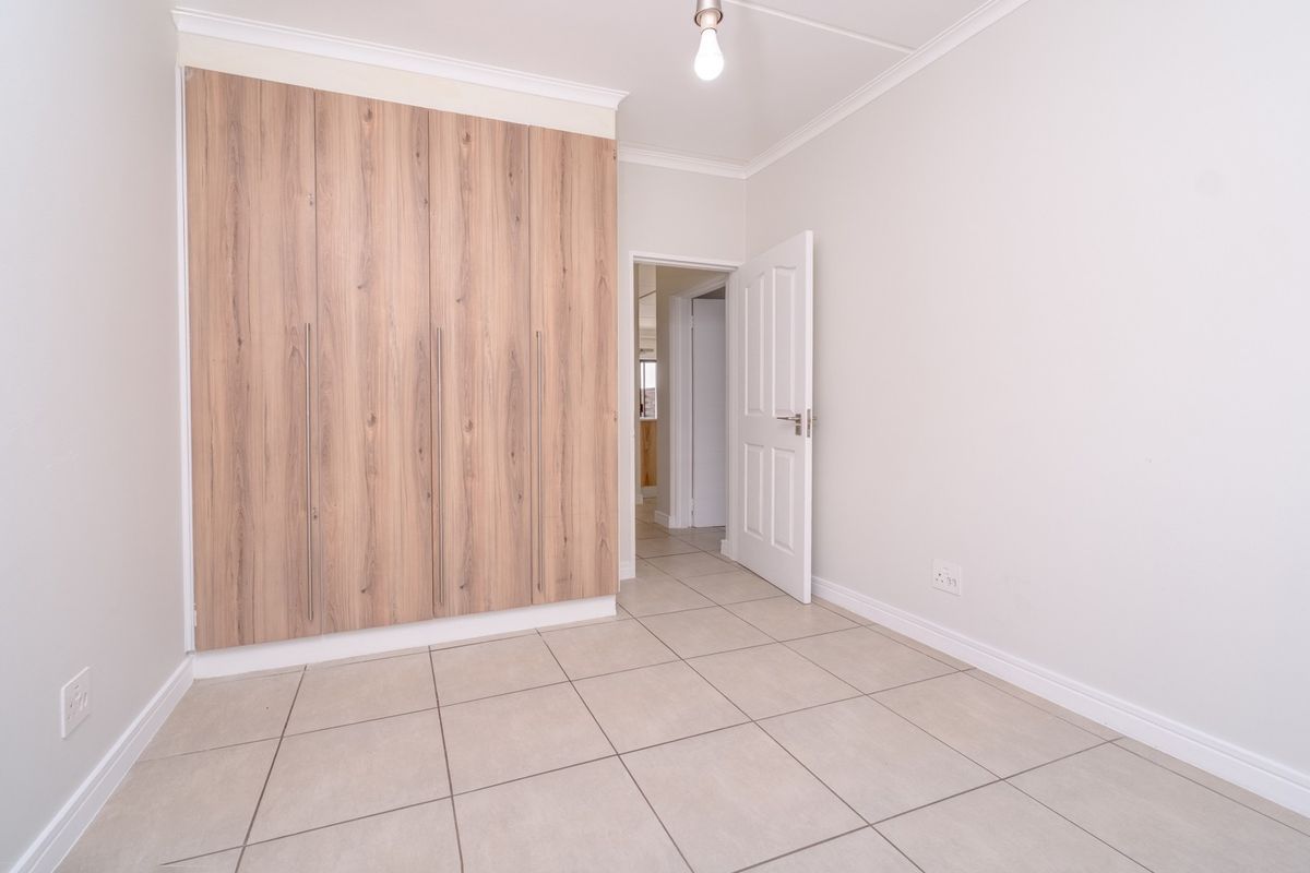 A clean, empty bedroom featuring modern wood-finish built-in cupboards, neutral tiled flooring, and coved cornicing, offering a bright and versatile living space.
