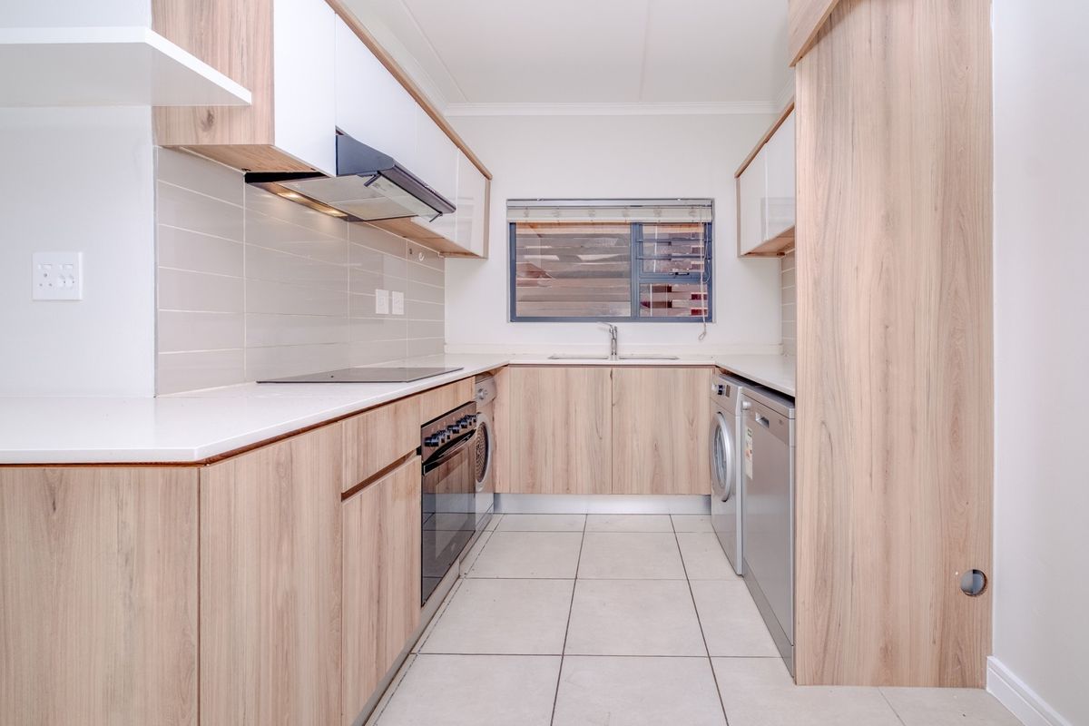 Modern galley-style kitchen featuring light wood-grain cabinetry, quartz countertops, integrated appliances, and tiled flooring in a clean, well-maintained space.