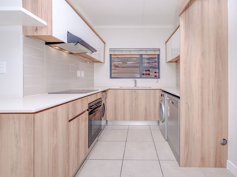 Modern galley-style kitchen featuring light wood-grain cabinetry, quartz countertops, integrated appliances, and tiled flooring in a clean, well-maintained space.