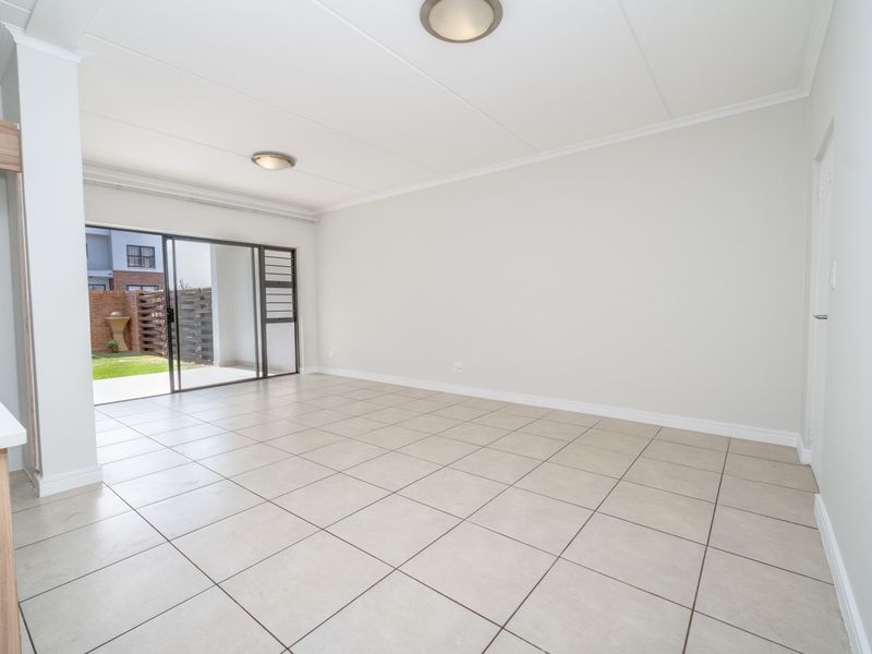 A bright, open-plan living area featuring neutral tiled flooring, flush mount lighting, and a sliding glass door providing direct access to the rear patio.
