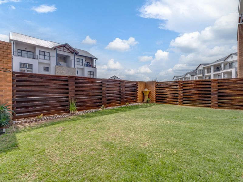A private rear garden featuring a well-maintained lawn, enclosed by timber slat fencing and brick boundary walls with a small water feature.