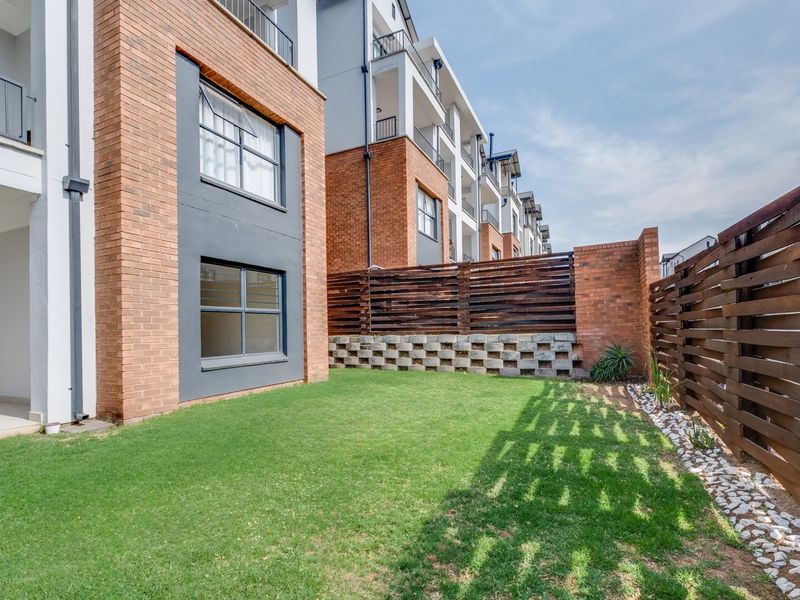 A private rear garden area featuring a well-maintained lawn, timber slat fencing, and a brick retaining wall, adjacent to the townhouse building facade.