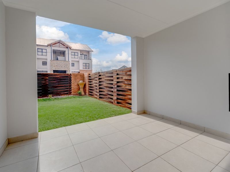 A covered patio area with tiled flooring, overlooking a private garden enclosed by wooden slat fencing and brick walls.