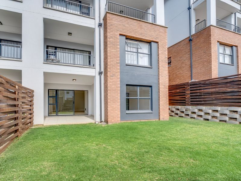 Rear view of a modern townhouse featuring a private garden, timber fencing, a covered patio, and upper-level balconies with brick and rendered finishes.