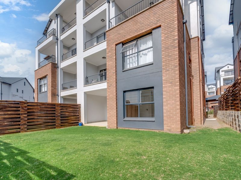 Rear view of a modern townhouse complex featuring brick and rendered facade, private balconies, and a well-maintained garden area with timber fencing.