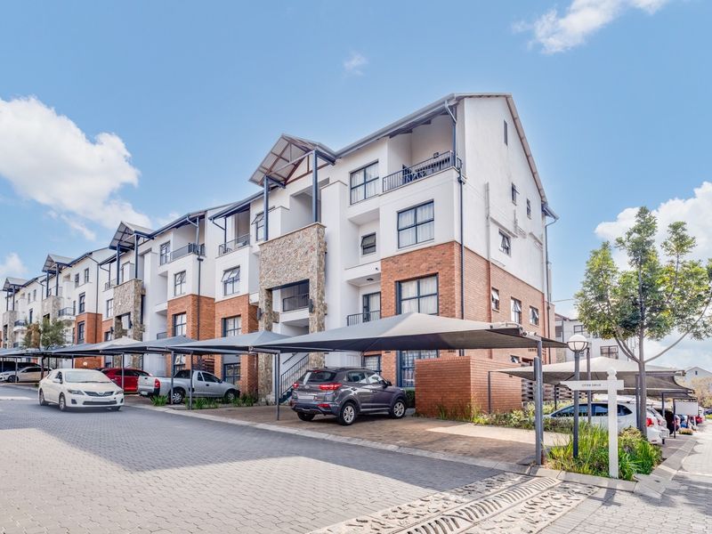 Front elevation of a multi-story townhouse complex featuring brick and stone facade details, paved driveway, and covered carport parking bays.