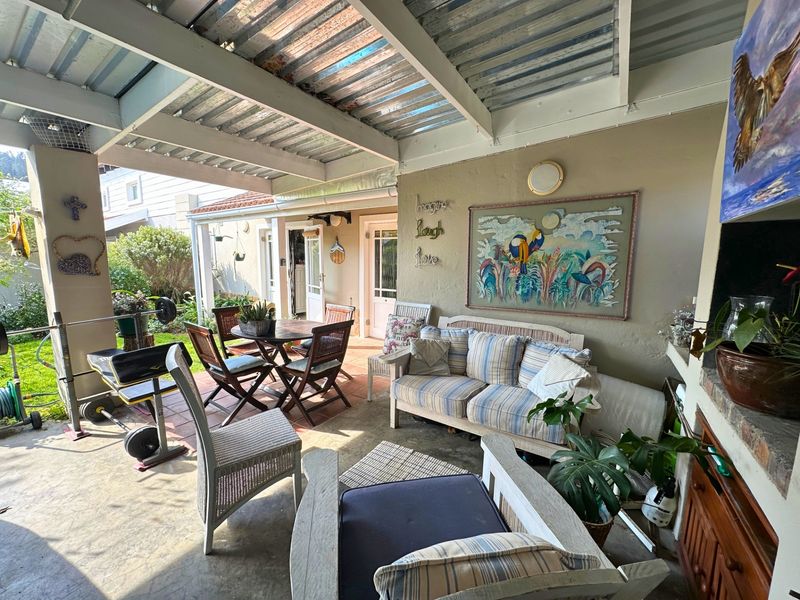 Covered outdoor patio area featuring a built-in brick braai, corrugated metal roofing, and direct access to the garden.