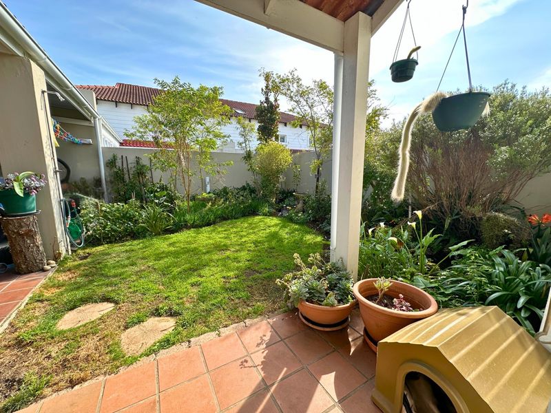 A covered patio area featuring tiled flooring, overlooking a private garden with established landscaping and boundary walls.