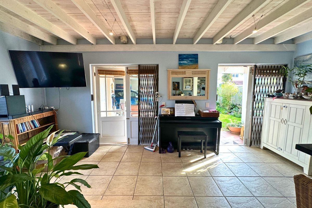 Living room featuring exposed beam ceilings, ceramic floor tiles, and dual access points to the garden through security-gated glass doors.